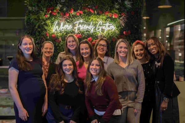 A group of guests gathered at Cork & Candles in front of the Where Friends Gather neon, with Ardmore franchisee Tia Holloway on the far right